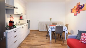 A modern kitchen with white cabinets, a dining area with a table and chairs, and a sofa with a red cushion. - Pordenone historic center (Pordenone)