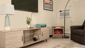 Una sala de estar con televisor, un cuadro enmarcado, un calentador pequeño y un sofá.