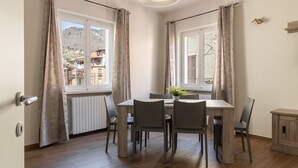 A dining area with a table and chairs, a radiator, and a view of buildings through the window. - Casa Marianna by Theater Home - located in the heart of Tignale with a marvellous lake view (Tignale)