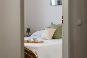 Ein Schlafzimmer mit Bett, Kissen, einem Nachttisch mit Lampe und einem Tablett mit Tassen und Teekanne.
