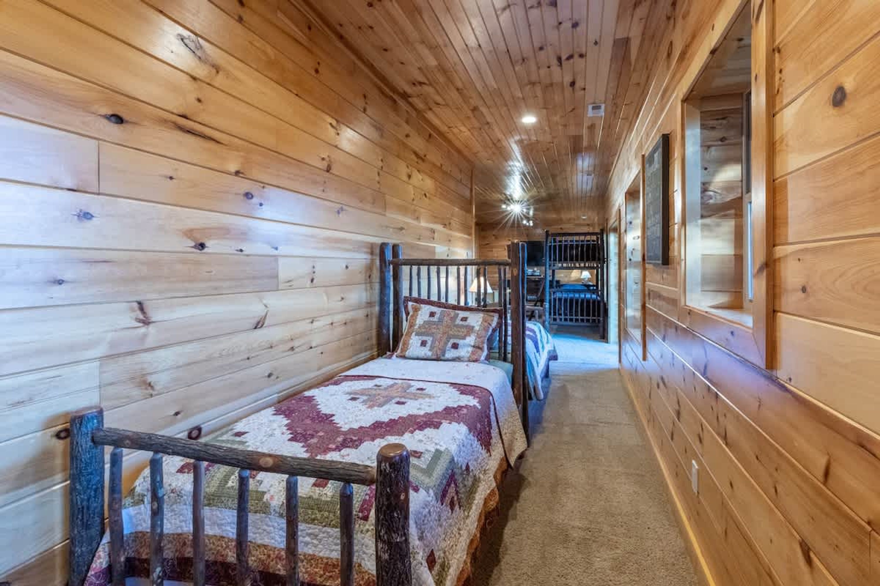 Un pasillo estrecho con paredes de madera y una cama con colcha.