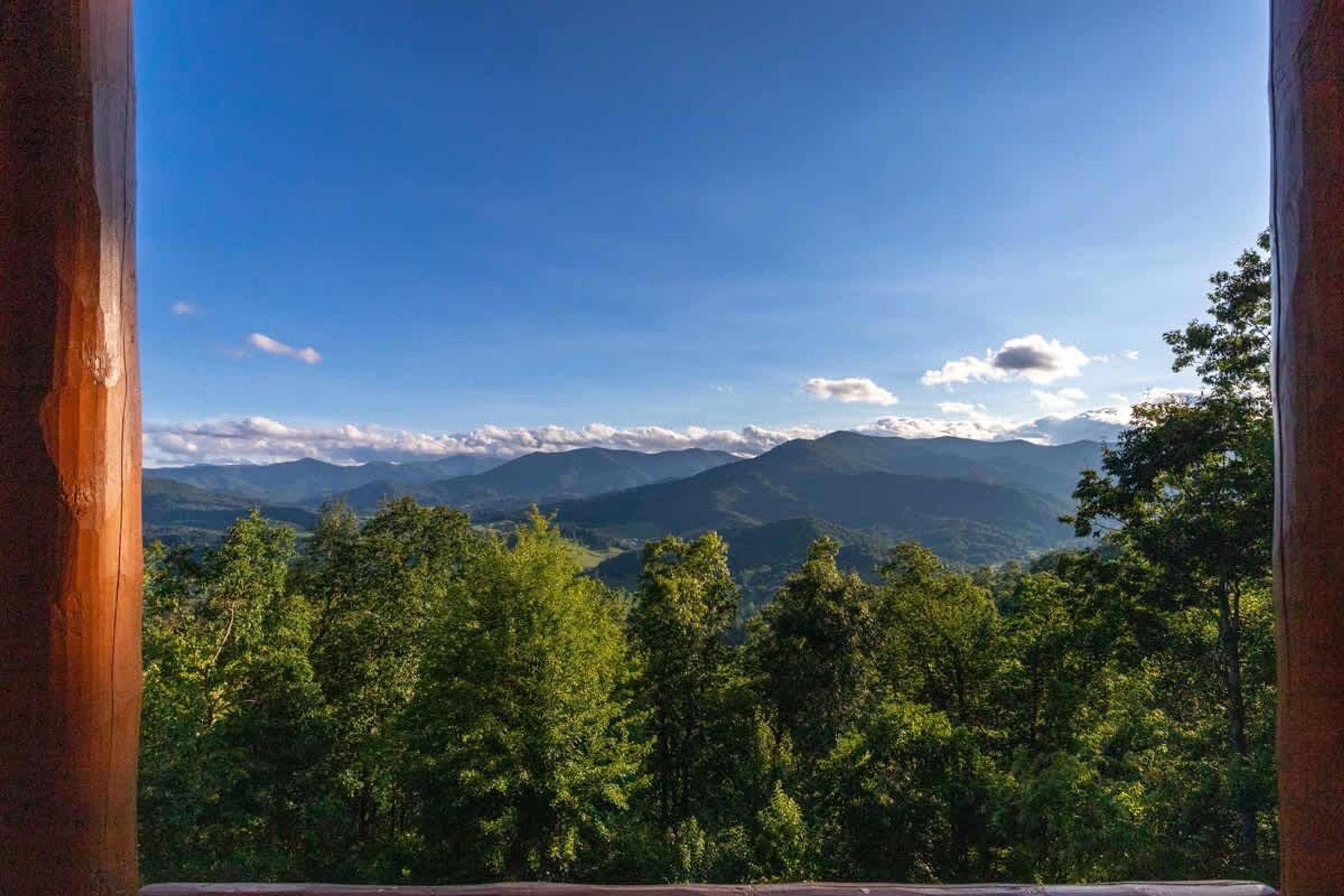 A view from a window overlooking a forested mountain range with a clear sky.