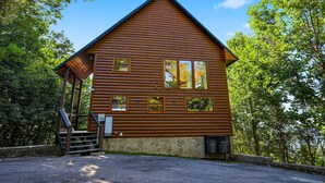 A log cabin with a stone foundation, a porch with steps, and multiple windows. - Mountain Top Cabin With Views Hot Tub and Arcade (Sevierville)