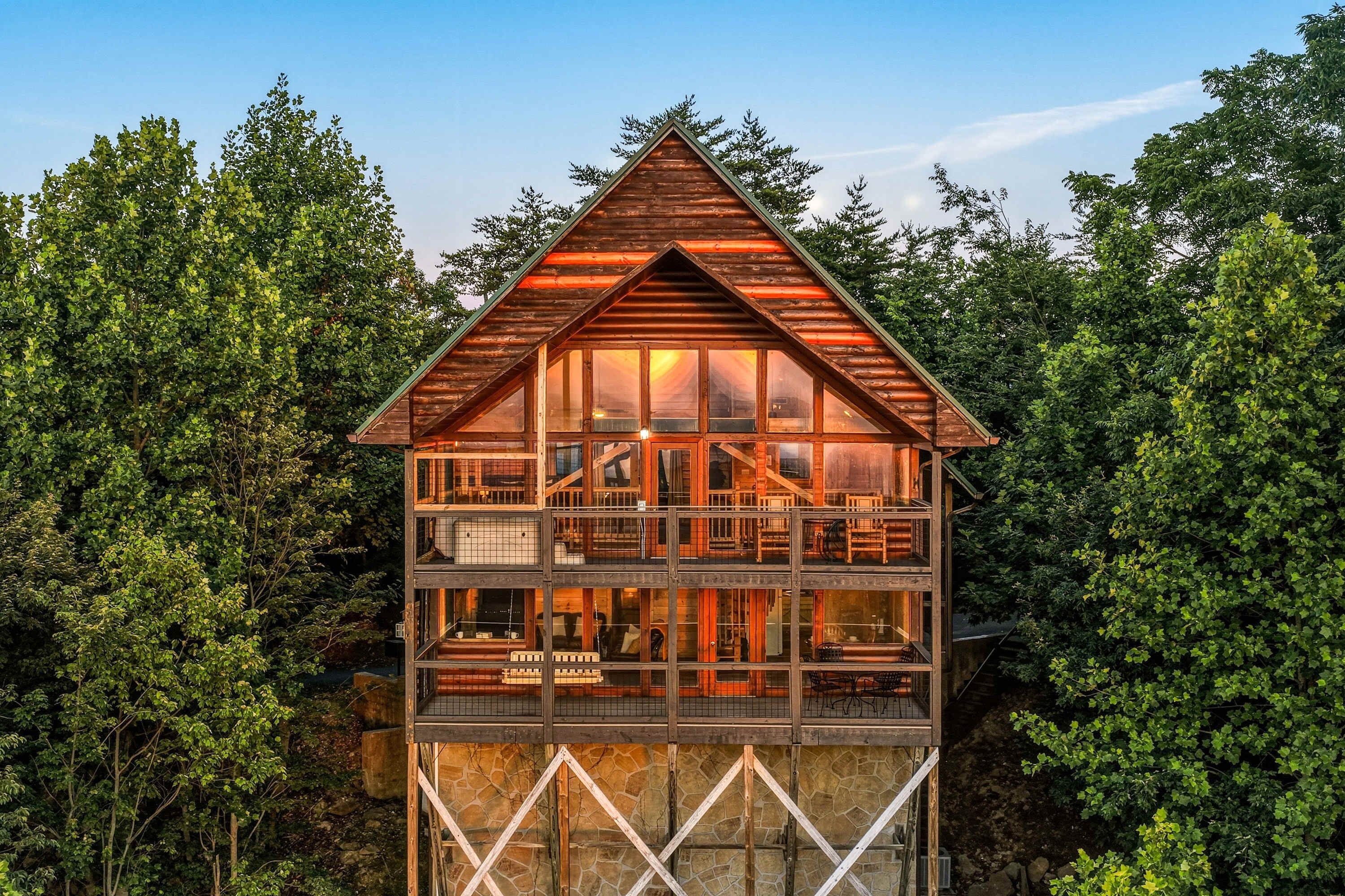 Una cabaña de madera de varios pisos con ventanas amplias, rodeada por un bosque denso.
