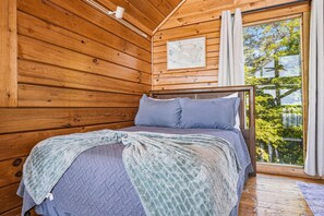 A wooden cabin bedroom with a bed, a window with curtains, and a framed picture on the wall. - Mountain Top Cabin With Views Hot Tub and Arcade (Sevierville)