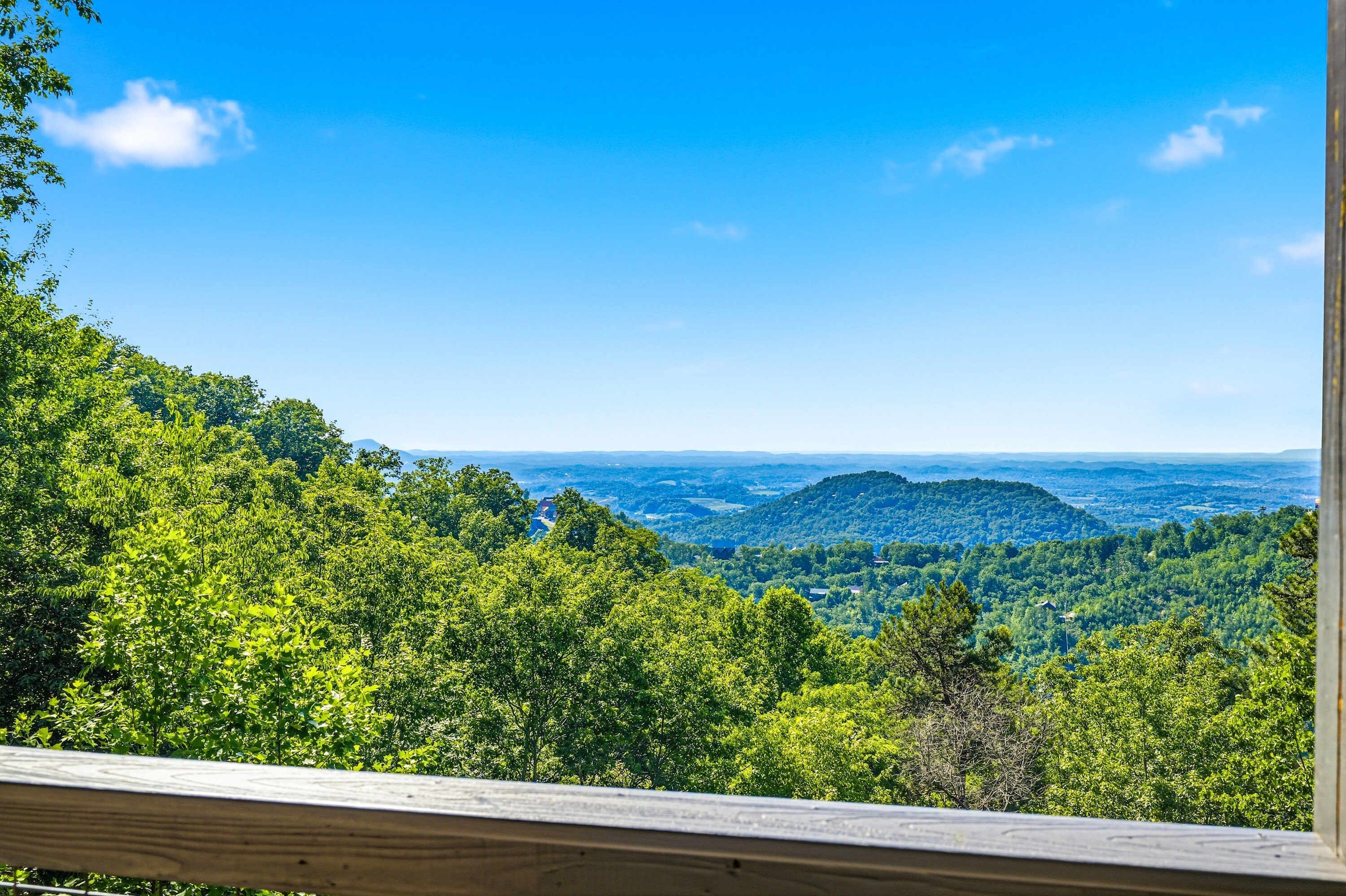A view from a wooden deck overlooking a forested mountain landscape with clear skies.
