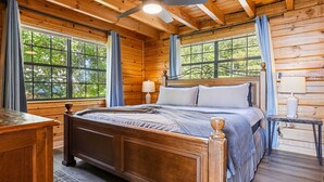 A wooden cabin bedroom with a bed, a ceiling fan, and large windows. - Mountain Top Cabin With Views Hot Tub and Arcade (Sevierville)