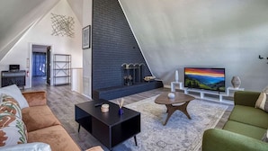 A modern loft apartment with a high ceiling, a fireplace, a television, and a cozy seating area. - 4BR 3BA Cabin w Games Hot Tub Near Smoky Mtns (Kodak)