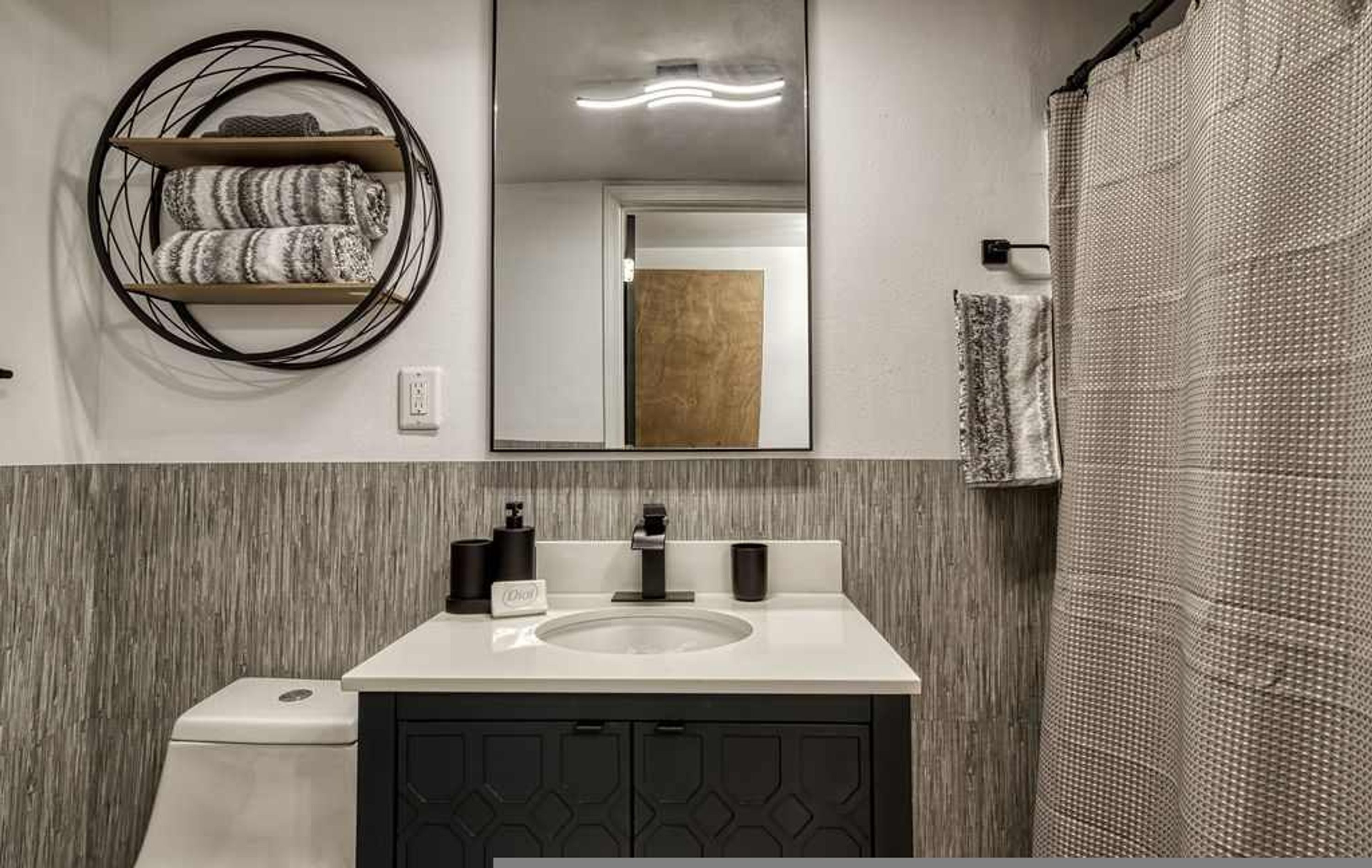 A modern bathroom with a white sink, black cabinets, a round mirror, and a shower curtain.