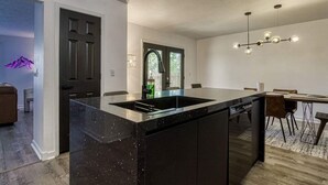 A modern kitchen with a large island, dark cabinetry, and a pendant light. - 4BR 3BA Cabin w Games Hot Tub Near Smoky Mtns (Kodak)