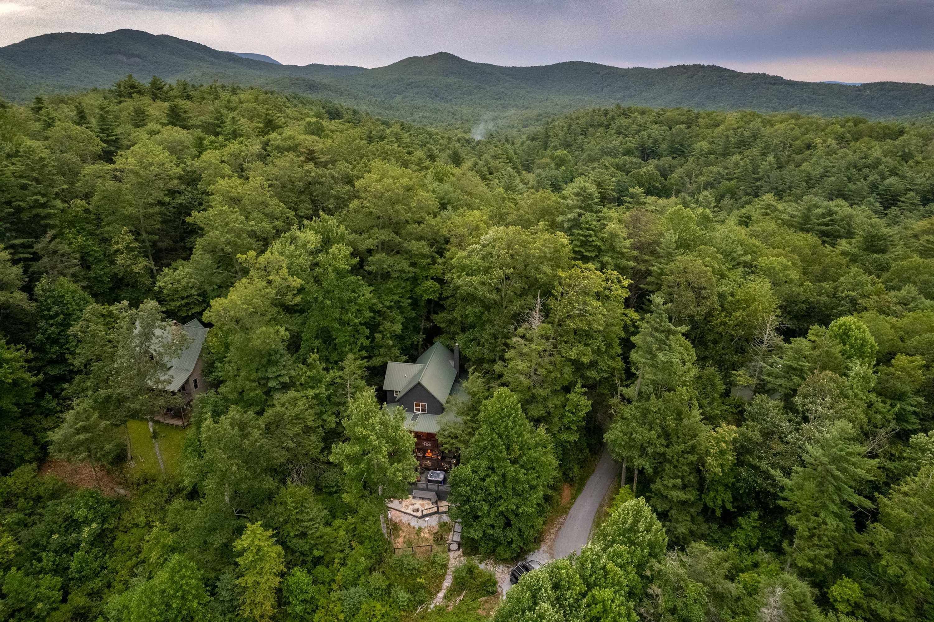 An aerial view of a secluded cabin surrounded by dense forest, with a clear path leading to the entrance.