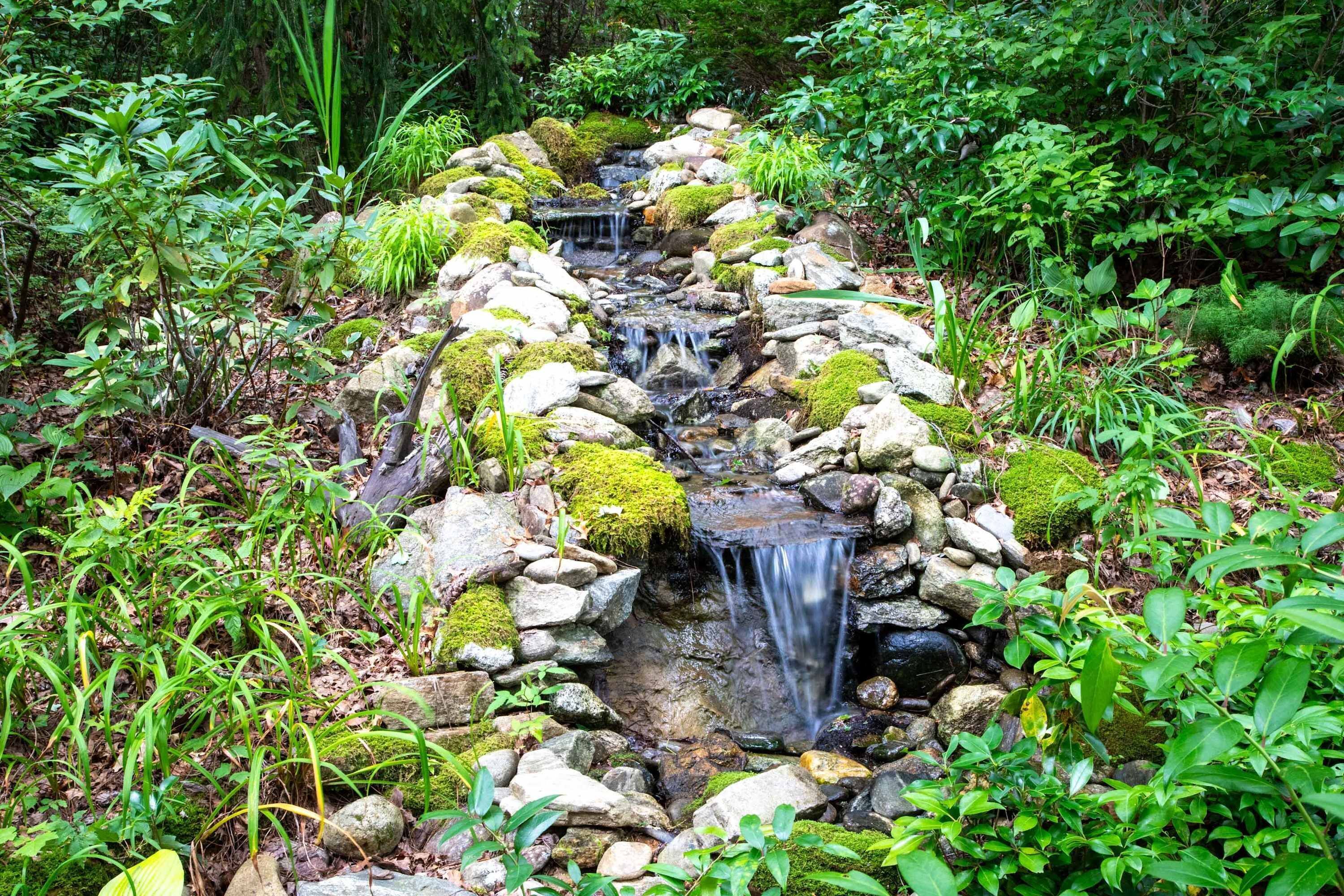 Una cascada pequeña en un jardín exuberante, con rocas y musgo.
