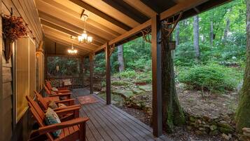 A covered porch with wooden benches and a view of a forested area.