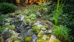 Ein friedlicher Garten mit einem kleinen Bach, einer Holzterrasse und einer Sitzgelegenheit.