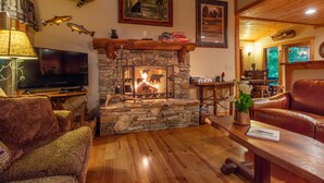 Ein gemütliches Wohnzimmer mit Kamin aus Stein, einem Fernseher und einer Ledersofa.
