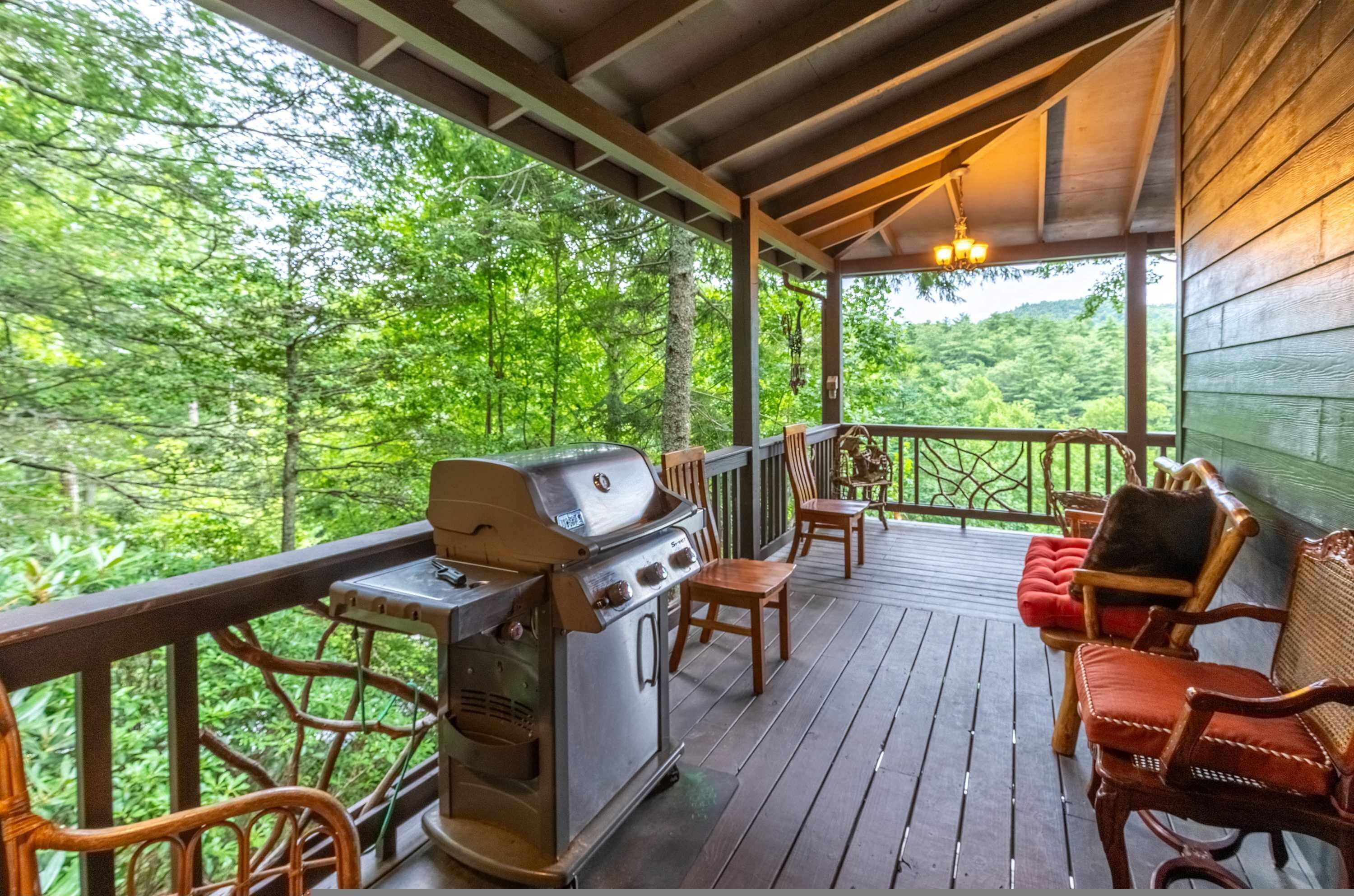 Eine überdachte Terrasse im Freien mit Grill, Holzstühlen und Blick auf einen Wald.