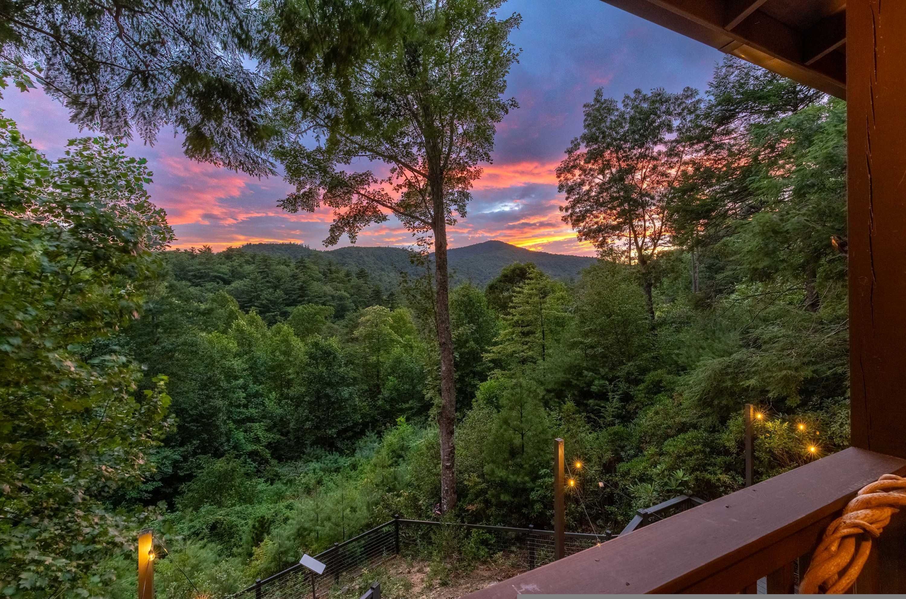 Une vue depuis un balcon donnant sur un paysage boisé, avec le soleil couchant à l’horizon.