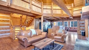 A spacious log cabin interior with a living area featuring leather sofas, a coffee table, and a kitchen in the background. - Secluded 7BR Mountain Escape on 7 Acres (Sevierville)