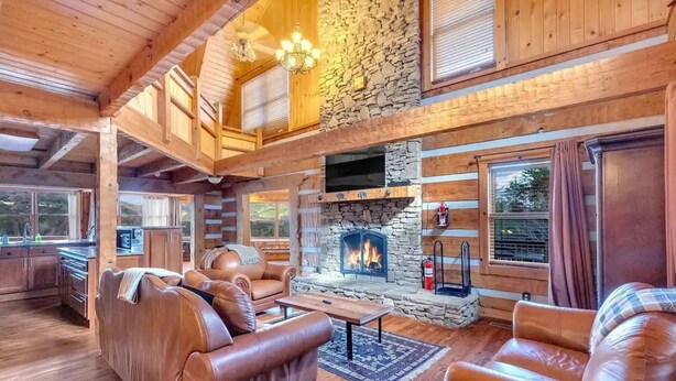 A log cabin interior with a stone fireplace, leather seating, and wooden beams. - Secluded 7BR Mountain Escape on 7 Acres (Sevierville)