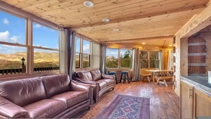 A room with a wooden ceiling, large windows, a leather sofa, a dining table with stools, and a view of the outdoors. - Secluded 7BR Mountain Escape on 7 Acres (Sevierville)