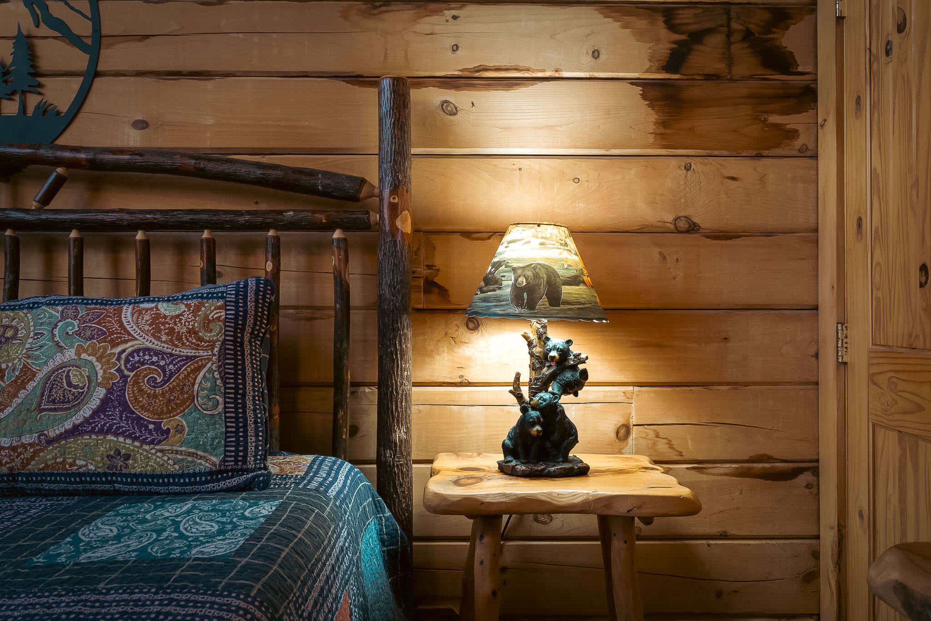 Interieur van een houten hutje met een bed, een lamp met een berendesign en een klein tafeltje.