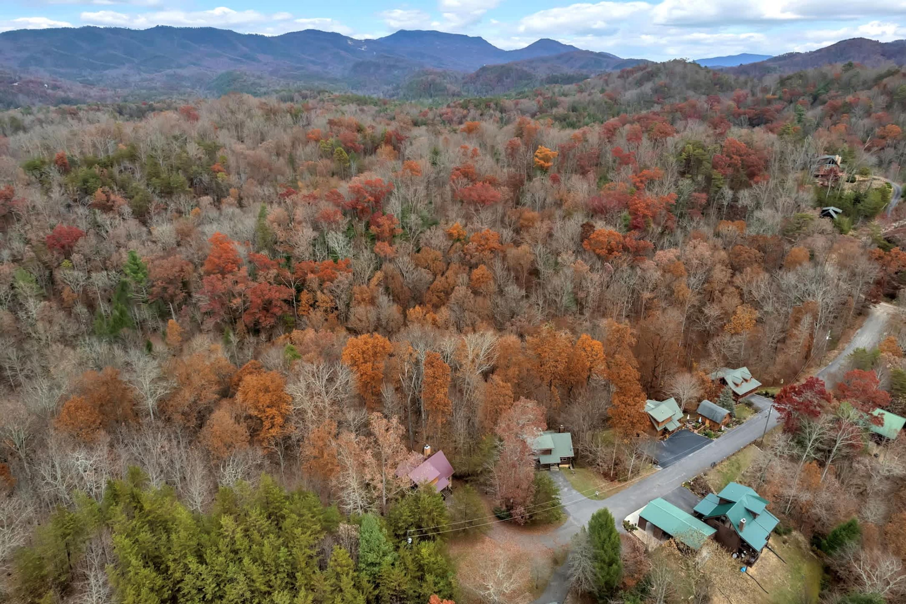 An aerial view of a forested area with several buildings, likely a resort or lodge, surrounded by autumn-colored trees.