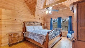 Ein Schlafzimmer in einer Holzhütte mit einem Bett, einem Nachttisch, einer Kommode und einem Deckenventilator.