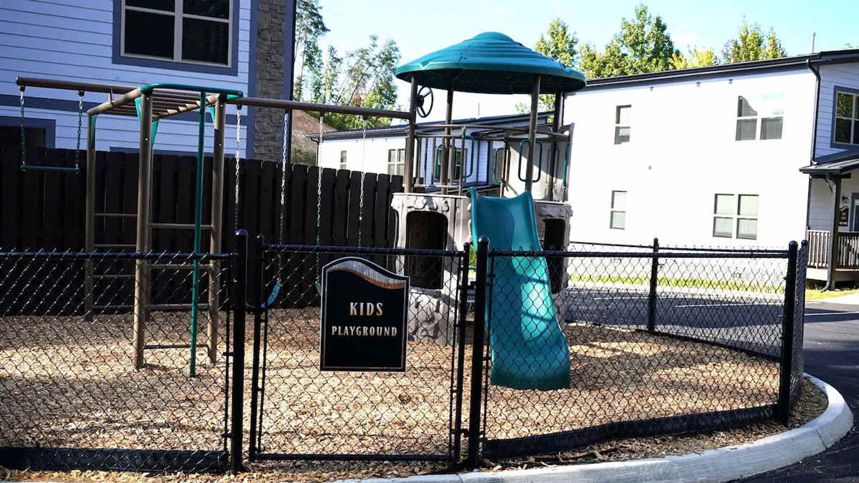 A fenced playground area with a swing set, a slide, and a play structure.