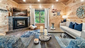 A cozy log cabin interior with a fireplace, a sofa, a coffee table, and a large window with curtains. - Modern 5 Bedroom Cabin Close-dollywood Game Room (Pigeon Forge)