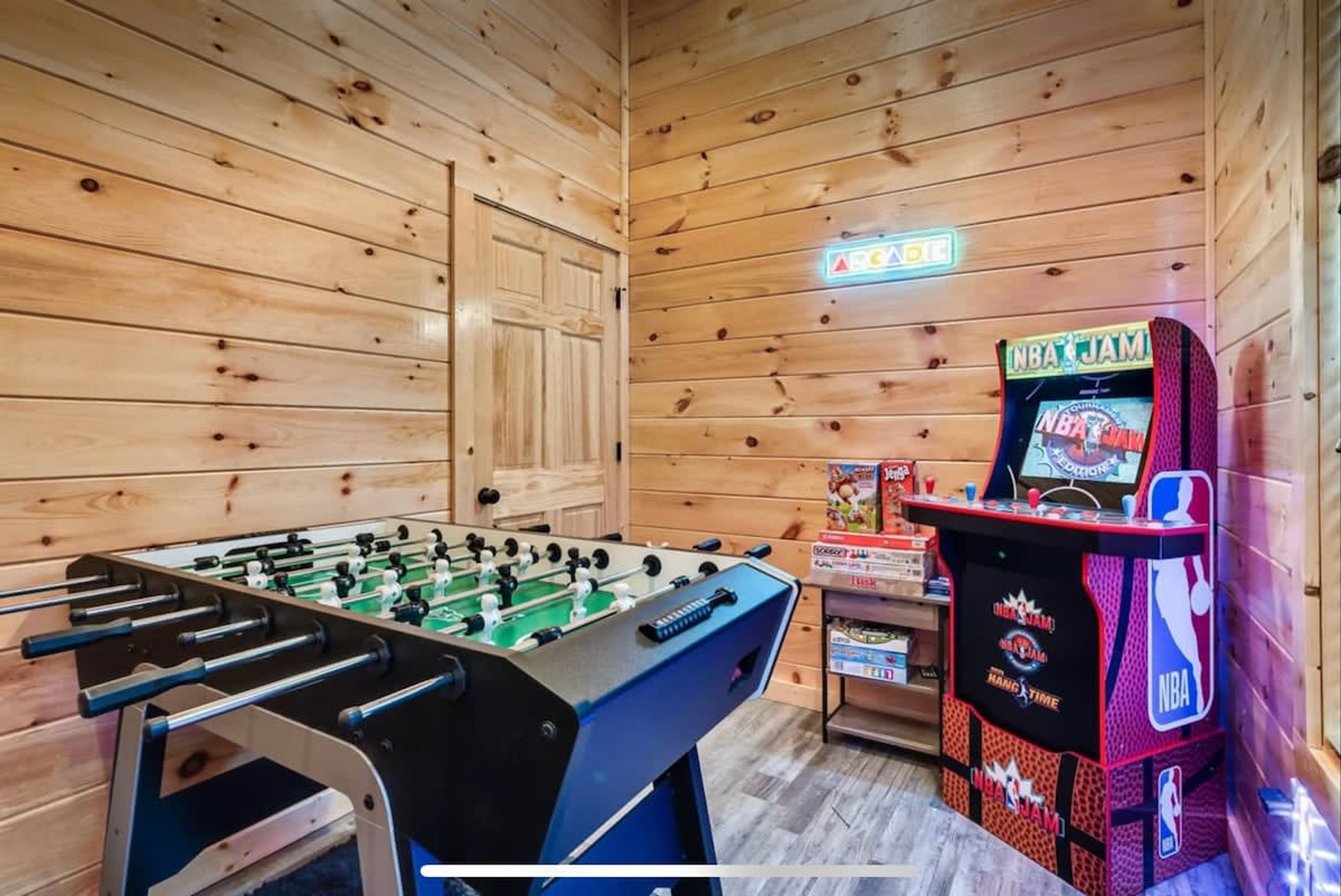 A room with a foosball table, an arcade machine, and wooden walls.