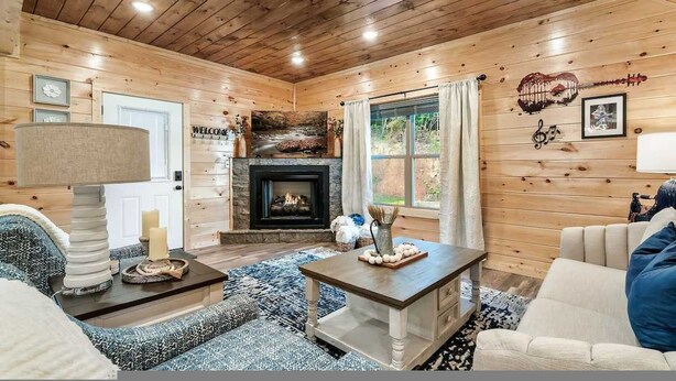 A cozy cabin-style room with a fireplace, wooden walls, and a large window. - Modern 5 Bedroom Cabin Close-dollywood Game Room (Pigeon Forge)
