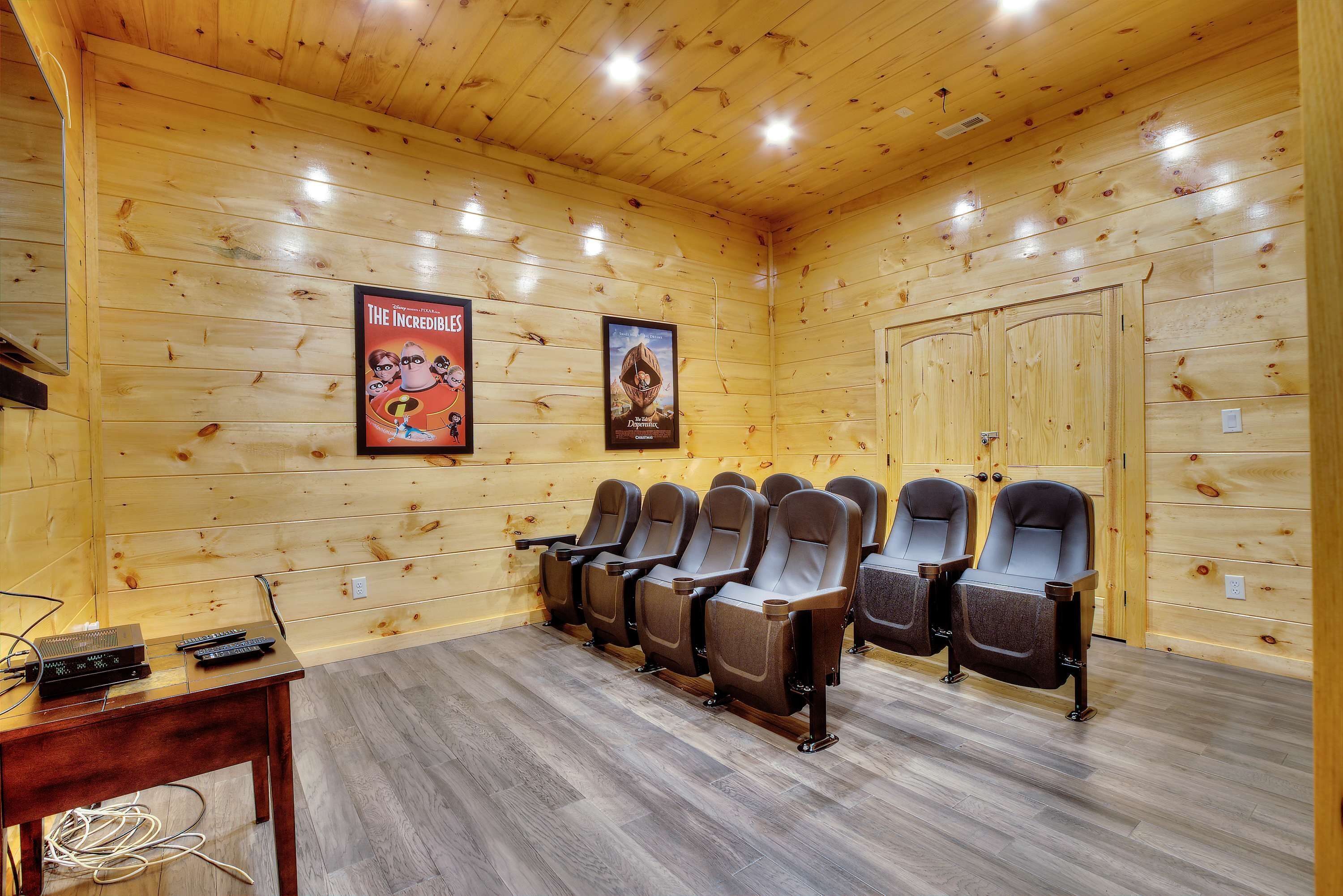 A wooden-paneled room with a row of reclining chairs, a small table with electronic devices, and two posters on the wall.