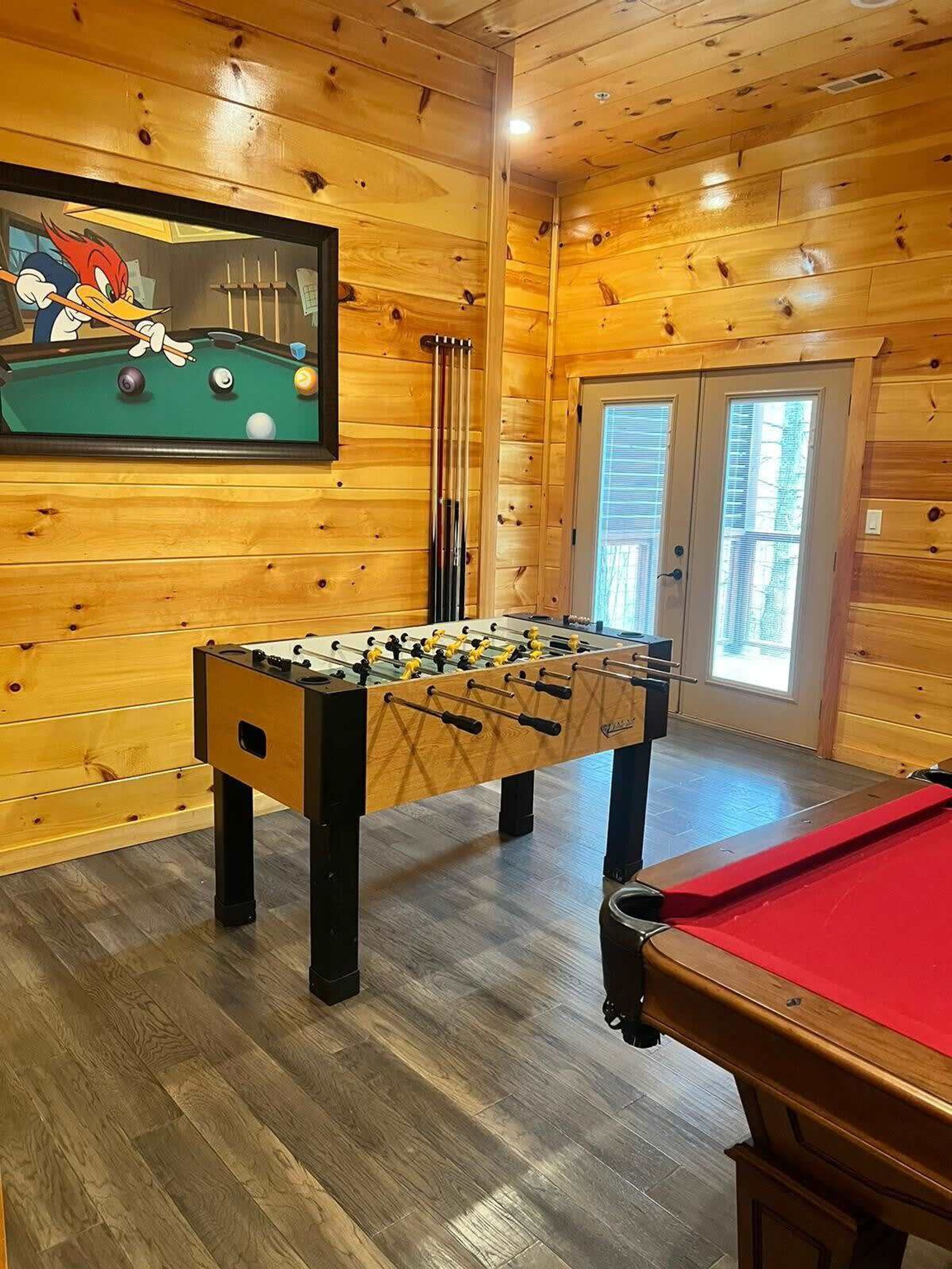 Ein Zimmer mit Holzboden, Kickertisch, Billardtisch und Poolbillardtisch.