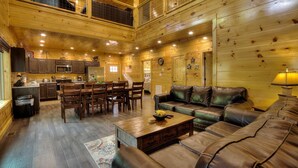 A spacious log cabin interior with a dining area, kitchen, and a large leather sofa. - New 5K Suites Hot Tub Game Room Near Gsmnp (Gatlinburg)