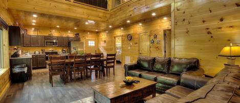 Un intérieur spacieux de chalet en bois, comprenant un coin repas, une cuisine et un grand canapé en cuir.