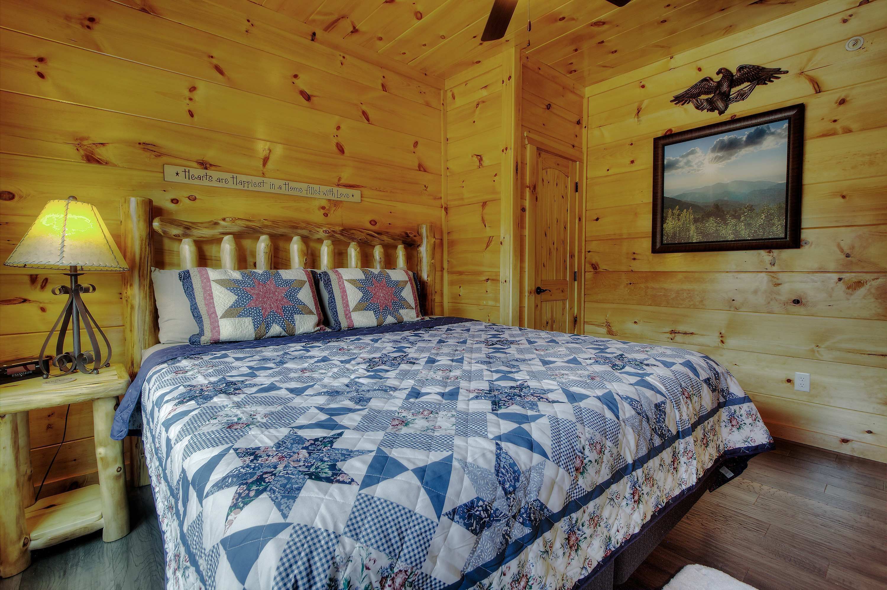 A wooden cabin room with a bed, a nightstand, a lamp, a framed picture, and a sign on the wall.
