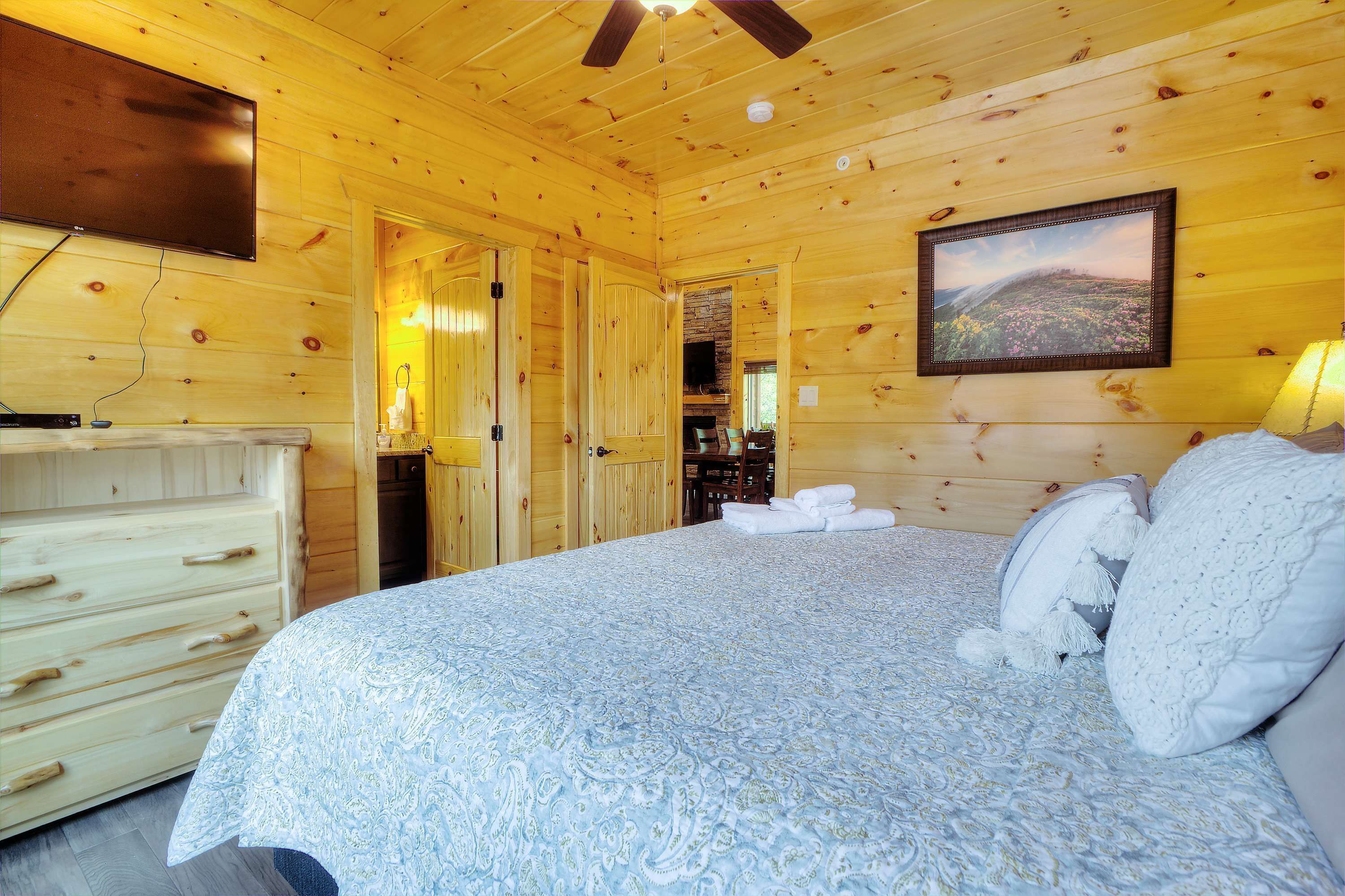 Un dormitorio de cabaña de madera con una cama, un tocador, un televisor y una chimenea.