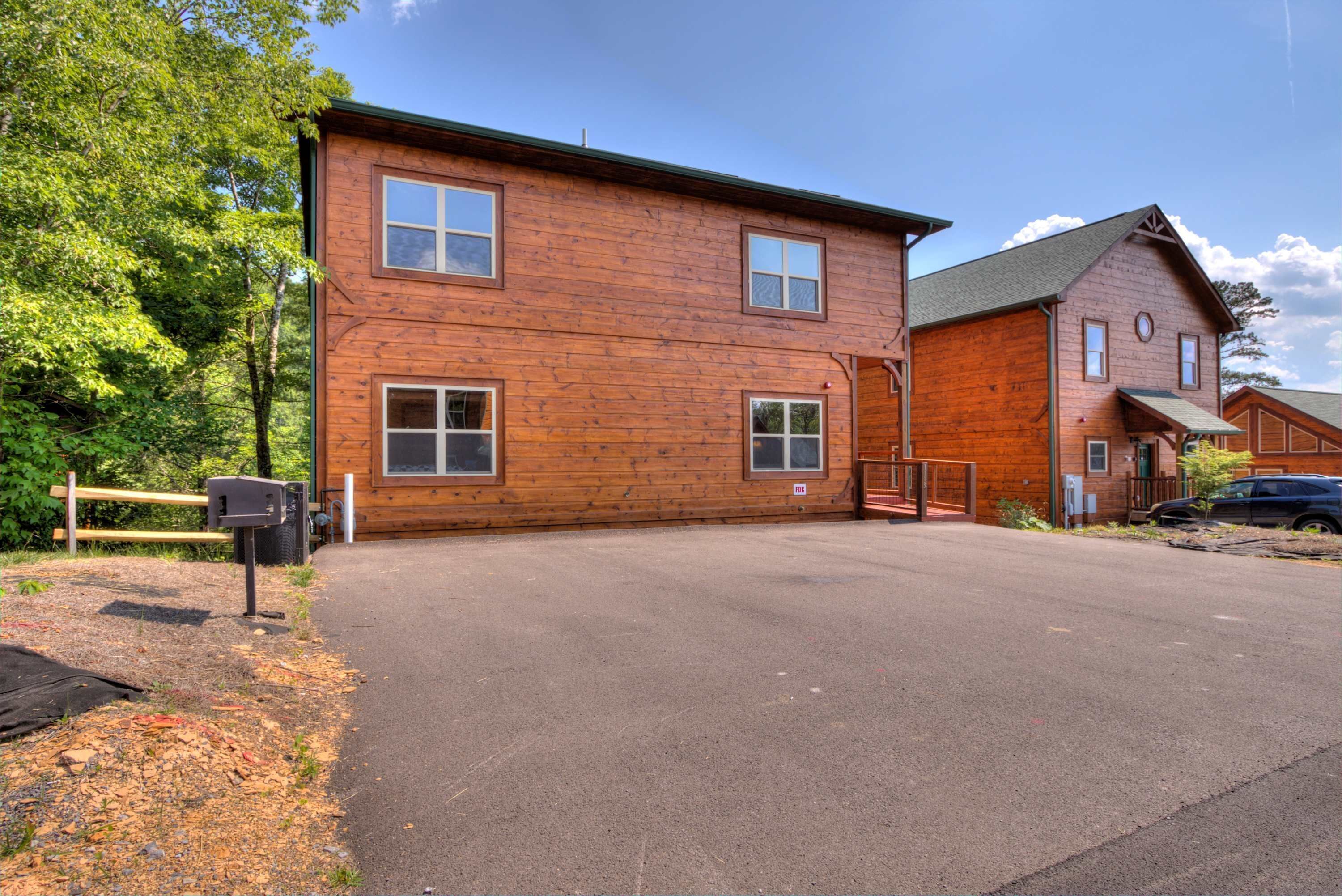 A two-story wooden cabin with a paved driveway and a mailbox.
