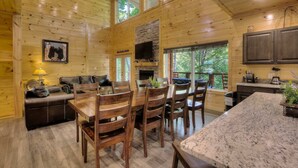 A wooden cabin interior with a dining area, kitchen, and a fireplace. - New 5K Suites Hot Tub Game Room Near Gsmnp (Gatlinburg)