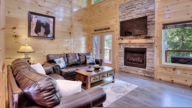 A cozy cabin interior with a leather sofa, a fireplace, and a stone accent wall. - New 5K Suites Hot Tub Game Room Near Gsmnp (Gatlinburg)