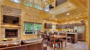 A spacious living area with a fireplace, a large TV, and a dining area with wooden furniture. - New 5K Suites Hot Tub Game Room Near Gsmnp (Gatlinburg)