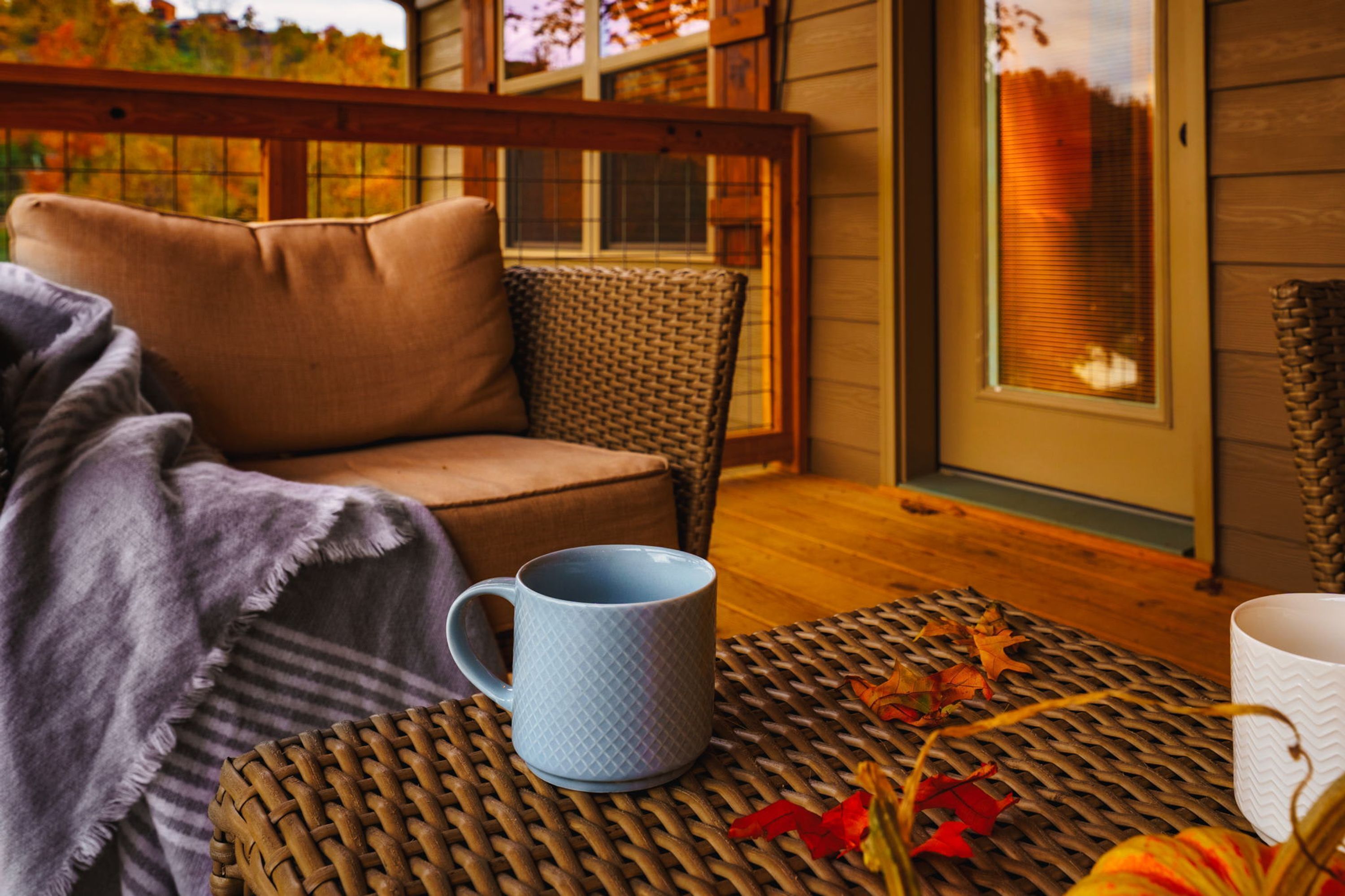 A cozy seating area with a wicker table, a blue mug, and autumn leaves.