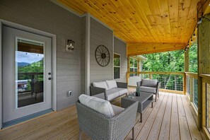 A covered porch with wicker furniture, a door with a view, and a wall clock. - Stunning 4 King Suites Hot Tub Views Gamerm (Gatlinburg)