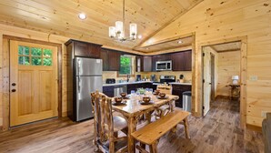 A wooden cabin interior with a dining table, chairs, a refrigerator, a microwave, and a sink. - Stunning 4 King Suites Hot Tub Views Gamerm (Gatlinburg)