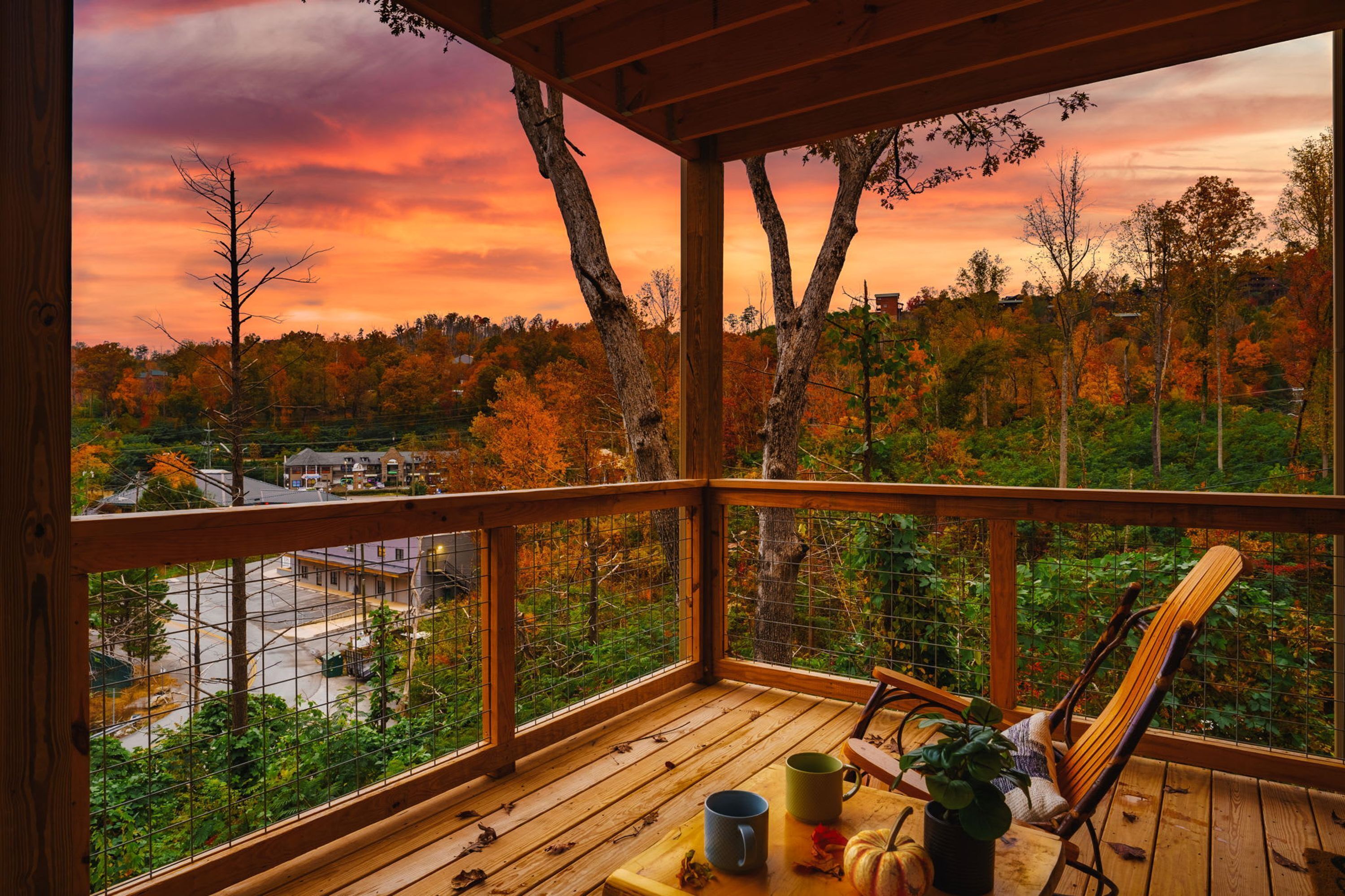 A wooden deck with a view of autumn trees and a sunset.