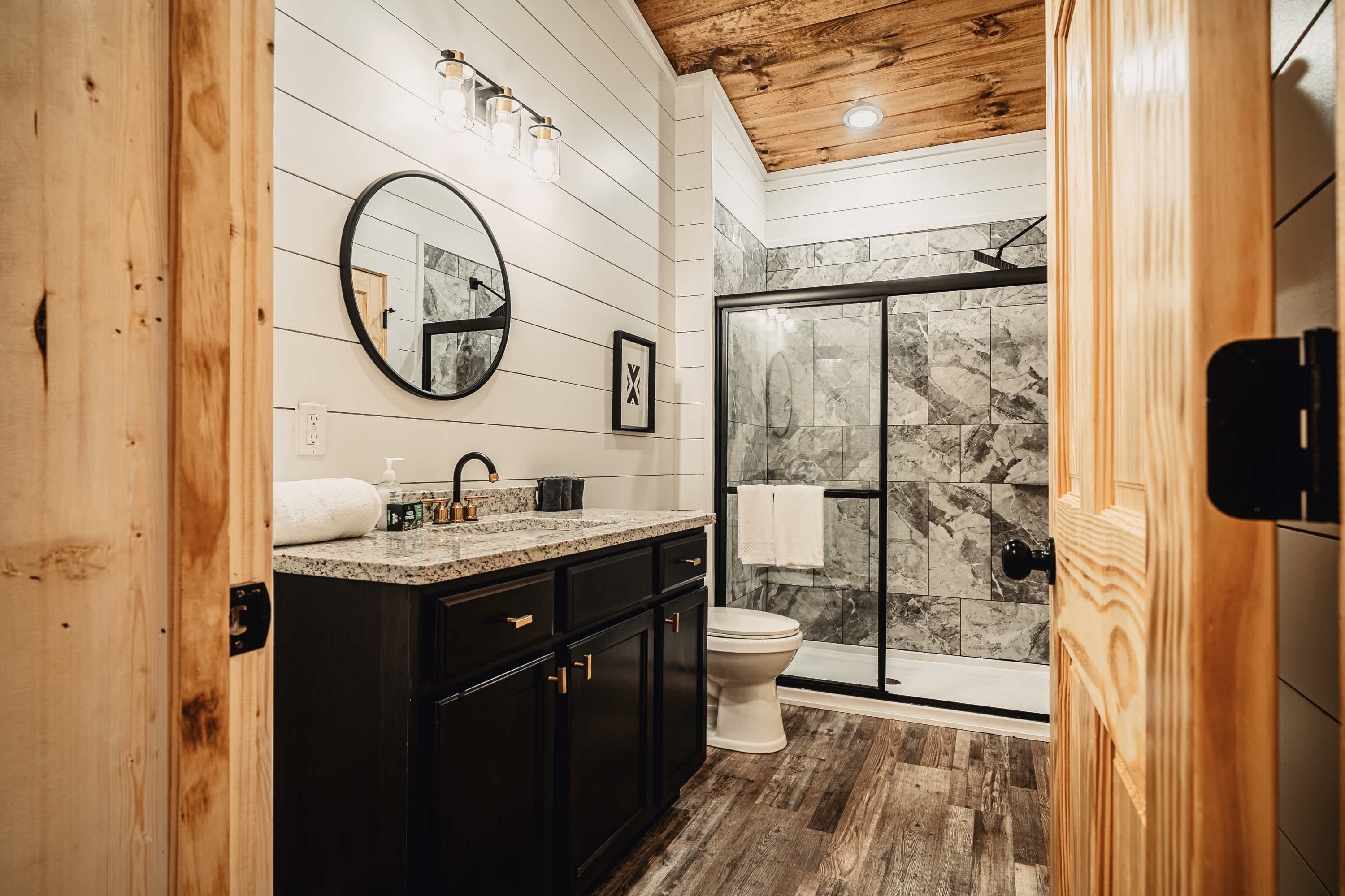 A bathroom with a wooden ceiling, a marble shower wall, and a black sink with a mirror above it.