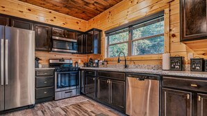 A modern kitchen with stainless steel appliances, dark wood cabinets, and a large window providing a view of the outdoors. - Stylish New 5BR 4BA Cabin Steps From Dollywood (Pigeon Forge)