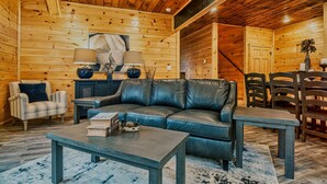 A cozy log cabin interior with a leather sofa, a dining table, and chairs. - Stylish New 5BR 4BA Cabin Steps From Dollywood (Pigeon Forge)