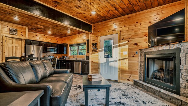 A cozy cabin interior with a leather sofa, a stone fireplace, and wooden walls. - Stylish New 5BR 4BA Cabin Steps From Dollywood (Pigeon Forge)