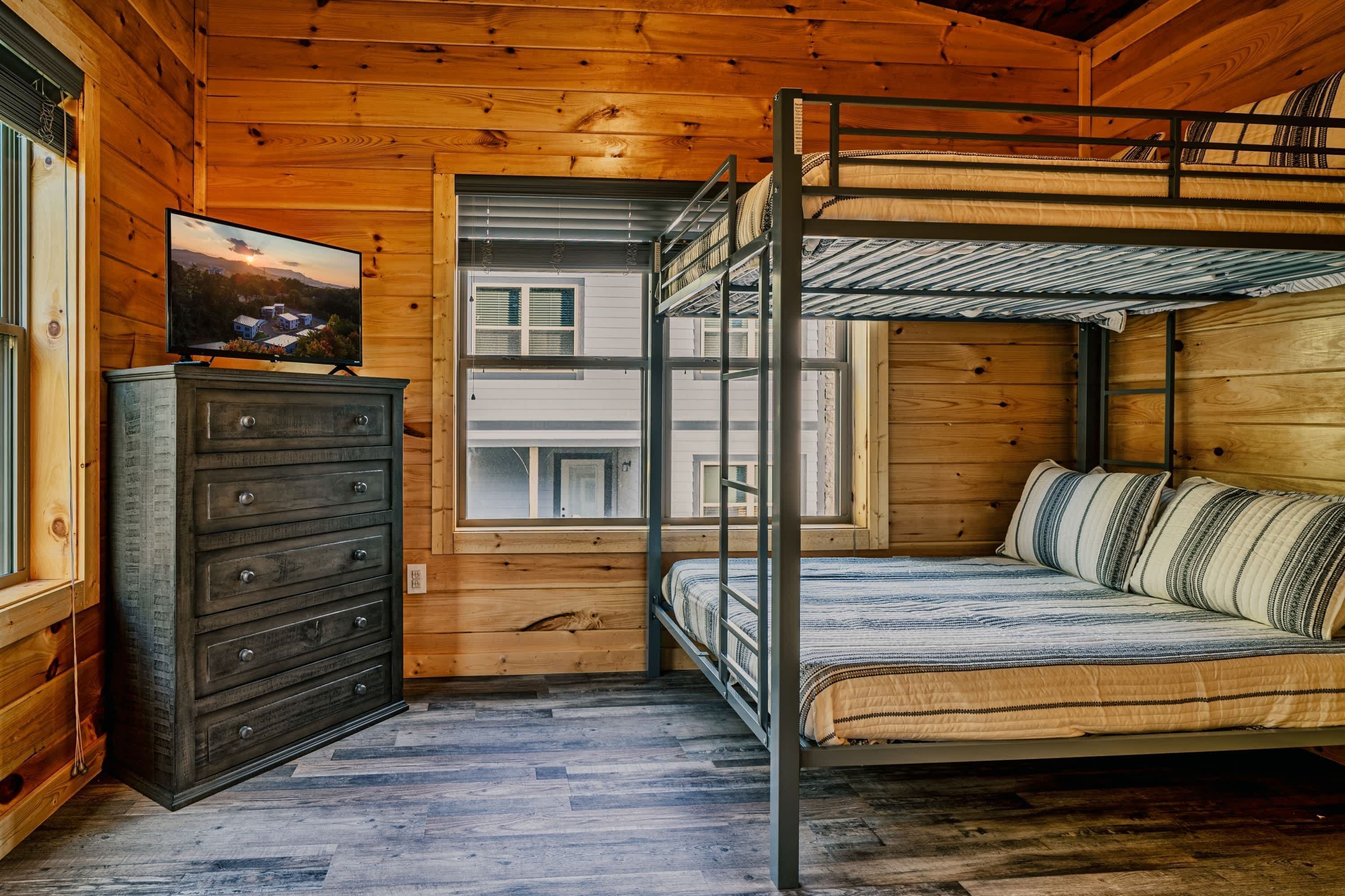 A bunk bed room with a dresser and a television on a wooden wall.